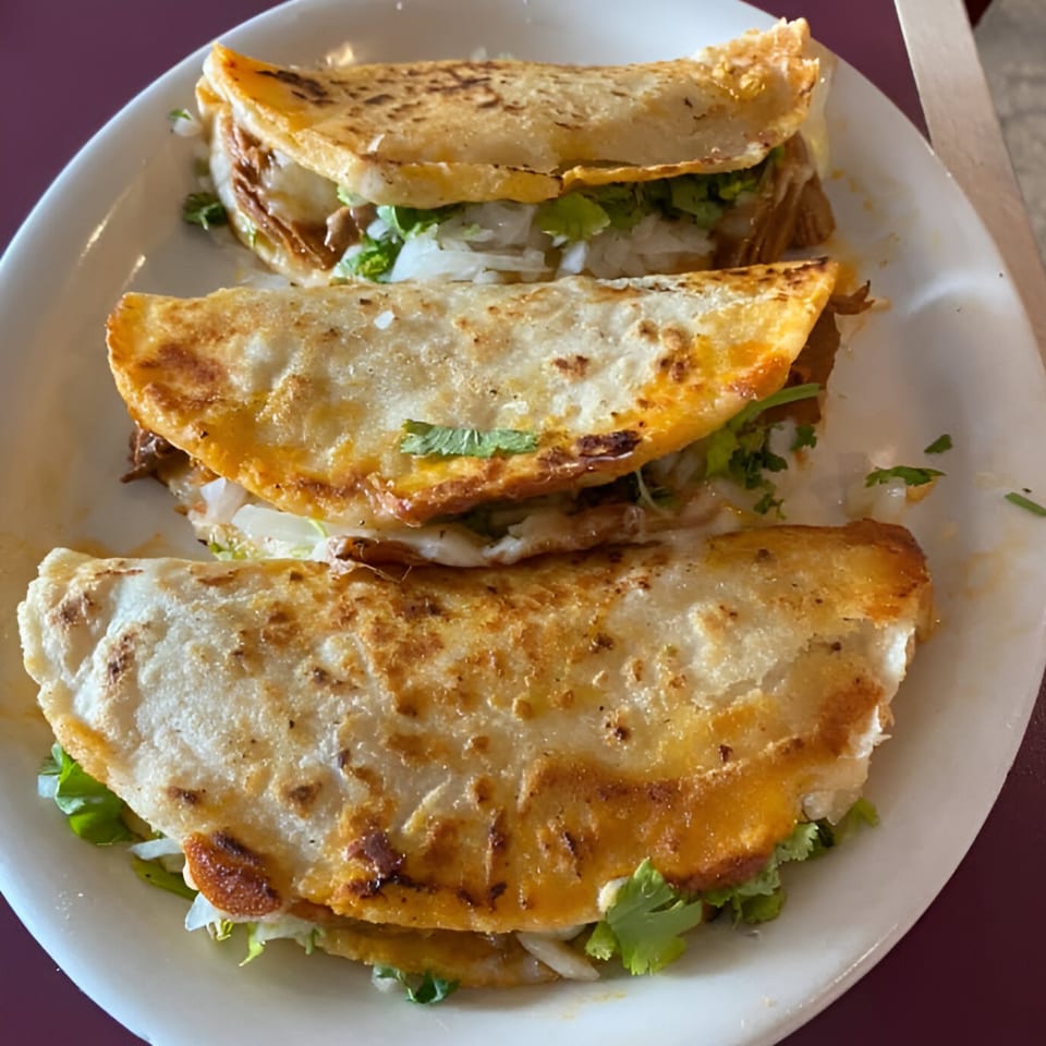 Three golden-brown quesadillas filled with meat, cheese, onions, and cilantro on a white plate.