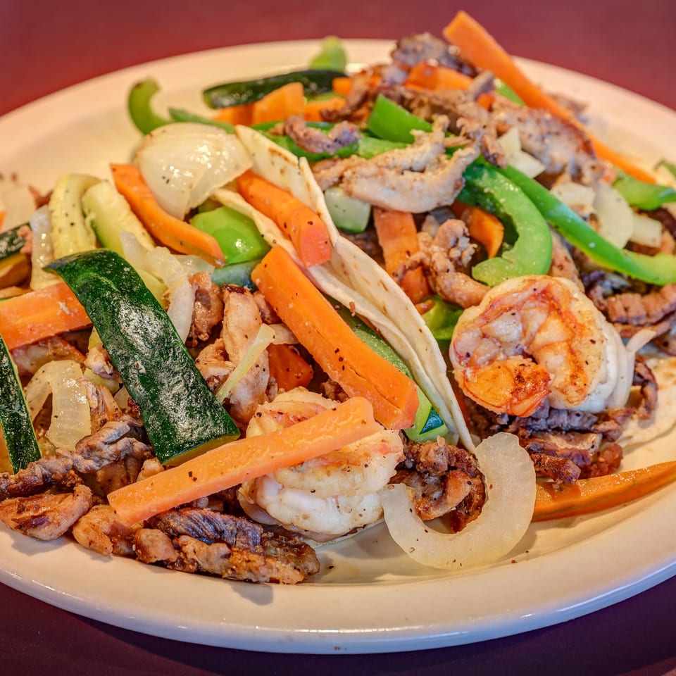 Casa Mexicana's sizzling fajitas with steak, shrimp, chicken, and colorful vegetables on a white plate.