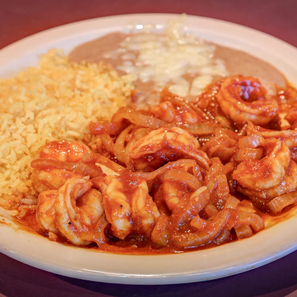 Casa Mexicana's Camarones a la Diabla, spicy shrimp with rice and refried beans on a white plate.