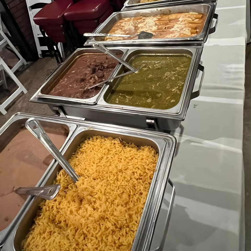 Buffet line with trays of Mexican food including rice, beans, green chili, and enchiladas.