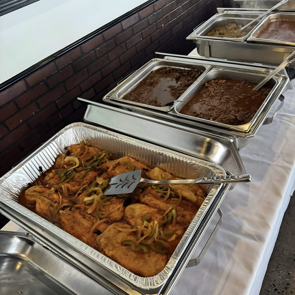 A buffet line with multiple chafing dishes filled with Mexican food, including meat and a dish with onions and peppers.