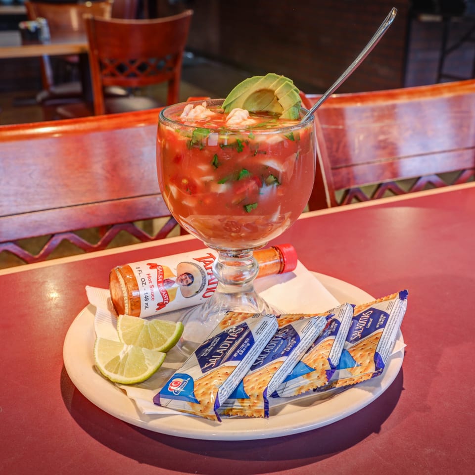 Shrimp cocktail with avocado, lime, hot sauce, and crackers on a white plate at Casa Mexicana.