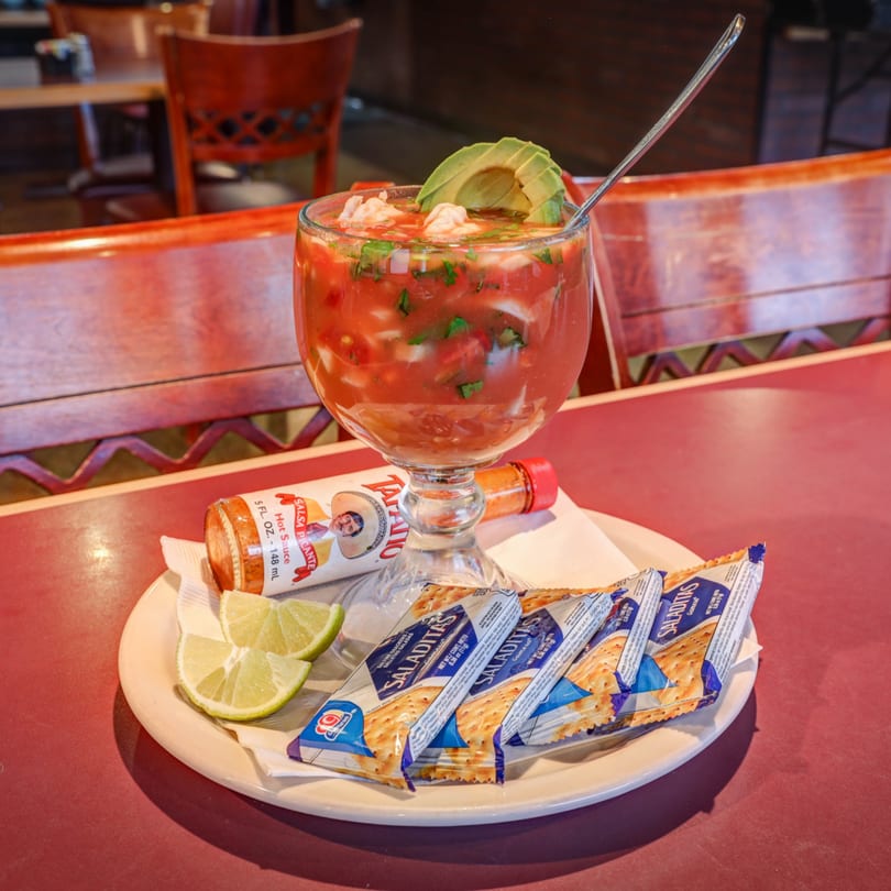 Shrimp cocktail with avocado, lime, hot sauce, and crackers on a white plate at Casa Mexicana.